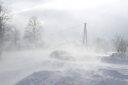 一辆汽车在一条覆盖着雪的危险道路上滑行。 私人交通正在与冬季因素作斗争。 暴风雪期间交通困难。寒冷天气的后果。