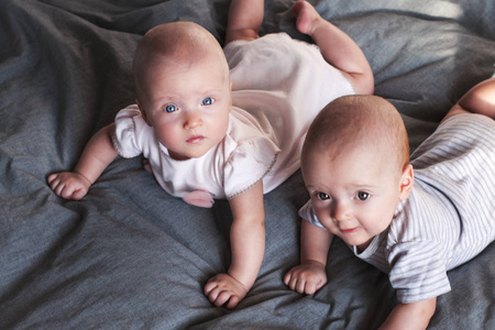 两个可爱的宝贝, 一个男孩和一个女孩在灰色背景的床上玩耍。哥哥和妹妹双胞胎。选择性对焦