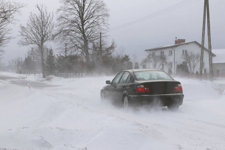 一辆汽车在一条覆盖着雪的危险道路上滑行。 私人交通正在与冬季因素作斗争。 暴风雪期间交通困难。寒冷天气的后果。