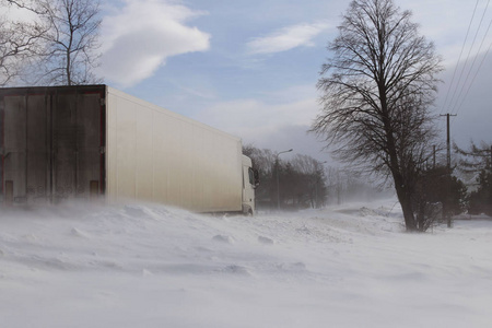 一辆大卡车在一条覆盖着雪的危险道路上偷偷地穿过雪堆。 蒂尔对抗冬季元素。 暴风雪期间交通困难。 寒冷天气和水的后果。