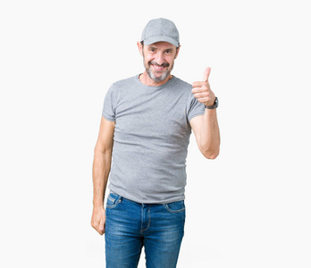英俊的中年老人戴着运动帽，在孤立的背景下，用手做快乐的拇指向上的手势。 赞许的表情看着相机显示成功。
