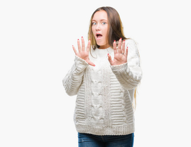 年轻美丽的高加索女人穿着冬天的毛衣,在孤立的背景下害怕和恐惧,表情