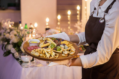 女服务员拿着一个木制的盘子,里面有肉和奶酪. 餐厅餐饮服务.照片