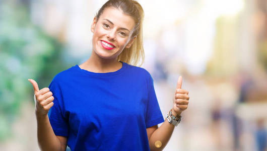 年轻漂亮的女人穿着休闲的蓝色T恤，在孤立的背景上，成功的标志，用手竖起大拇指，微笑和快乐地做积极的手势。 用欢快的表情看着相机，