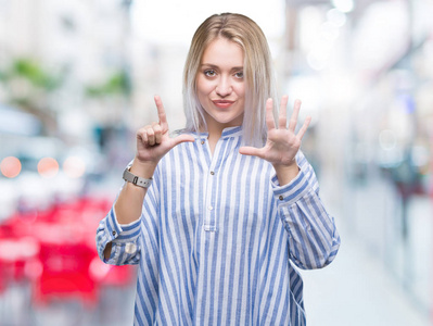 年轻的金发女子在孤立的背景显示和指向7号手指，同时微笑自信和快乐。