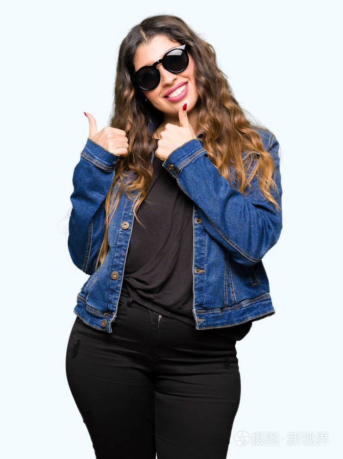 年轻漂亮的女人戴着太阳镜,用手做快乐的竖起大拇指的手势.