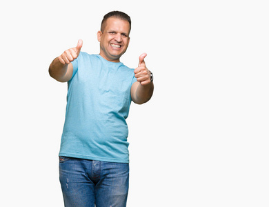 中年阿拉伯男人穿着蓝色T恤，在孤立的背景下，批准用手竖起大拇指做积极的手势，微笑，为成功而高兴。 看着相机赢家的手势。