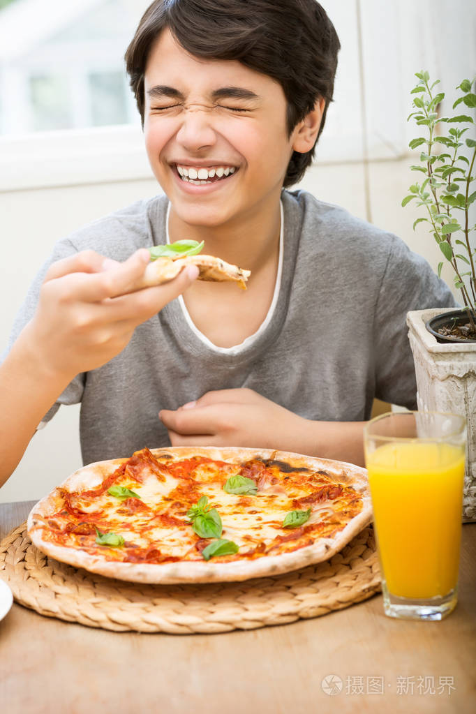 一个快乐的男孩的肖像快乐地吃披萨笑着快乐地享受美味的食物在家度过