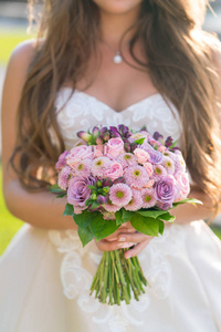 新娘拿着粉红色和淡紫色的婚礼花束的各种鲜花