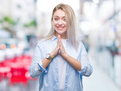 年轻的金发女人在孤立的背景下祈祷，双手一起请求宽恕，微笑自信。