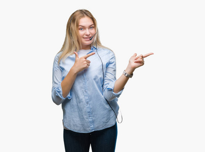 年轻的高加索商务女性戴着呼叫中心耳机，在孤立的背景上微笑，看着相机，双手和手指指向一边。