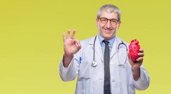 英俊的高级心脏病专家医生，男人抱着心，在孤立的背景下做OK标志，手指，优秀的符号