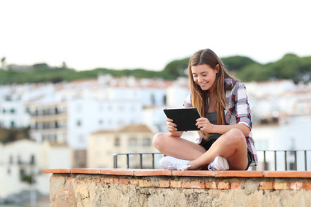 快乐的青少年女性在平板电脑上观看媒体，坐在城镇的窗台上