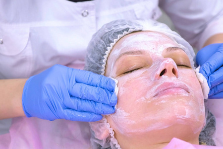 美容师用棉垫从面膜上洗掉女性的脸。特写镜头。去除遮罩