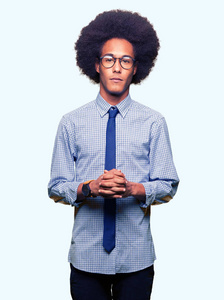 年轻的非裔美国商人带着非洲头发，戴着眼镜，双手和手指交叉着微笑，轻松愉快。 成功和乐观