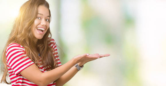 年轻漂亮的黑发女人，穿着条纹T恤，在孤立的背景上，用手和张开的手掌指向一边，呈现出微笑快乐和自信的广告
