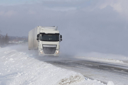 一辆大卡车在一条覆盖着雪的危险道路上溜过雪堆。轮胎对抗冬季元素。暴风雪期间交通困难.寒冷天气和水的后果。