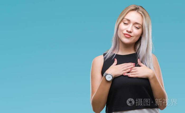 年轻的金发女子在孤立的背景上微笑,双手放在胸部,闭着眼睛,脸上有