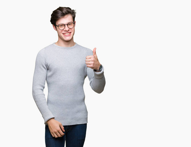 年轻的帅哥戴着眼镜在孤立的背景上做快乐的拇指向上手势与手。赞许的表情看着相机，显示出成功。