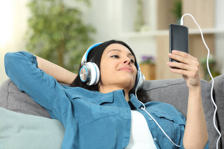 坐在家里客厅的沙发上，一个放松的女人在听智能手机上的音乐