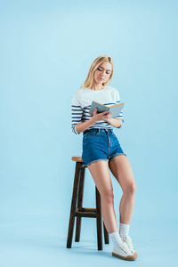 漂亮的年轻女子坐在椅子上，在蓝色背景上看书