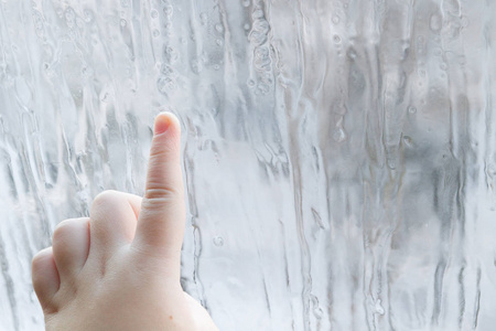 s hand draws patterns on the frozen window in winter