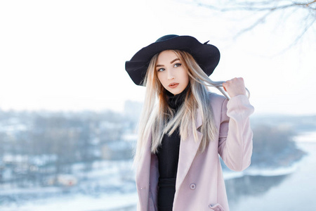 美丽的年轻女子，金色的头发，戴着一顶老式的帽子，穿着一件复古风格的冬季粉红色外套，站在外面的背景上，在一个冬天阳光明媚的日子