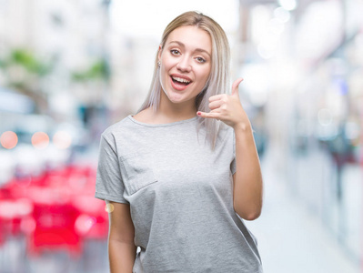 年轻的金发女人在孤立的背景上微笑着做电话手势，用手和手指，就像在电话上交谈。交流概念。