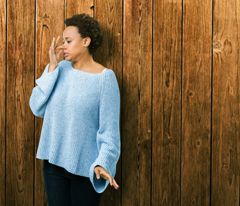 年轻美丽的非洲裔美国妇女穿着一件毛衣，在孤立的背景上闻到一些臭味和恶心，难以忍受的气味，用手指在鼻子上屏住呼吸。坏气味的概念。