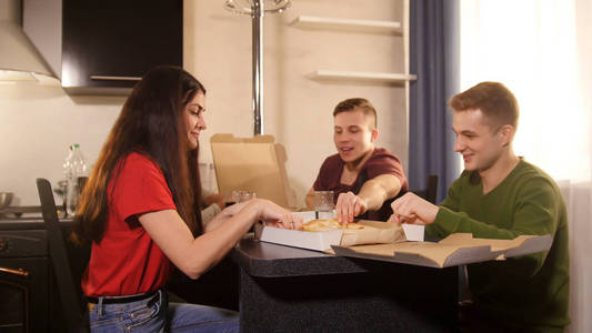 三个年轻人坐在厨房里吃披萨