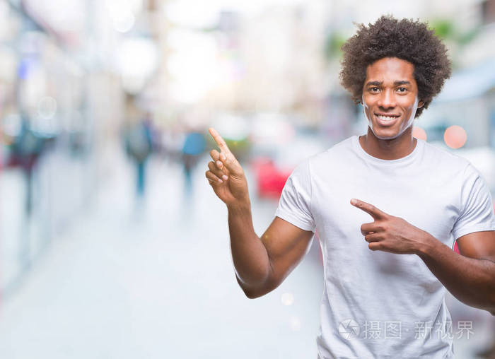 美国黑人男子在孤立的背景上微笑看着相机用两只手和手指指向一边