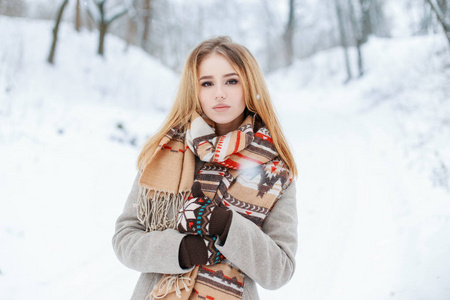 时尚的现代年轻女子穿着时尚的冬季保暖衣服，穿着羊毛手套在冬季森林里散步。美丽的女孩喜欢大自然。