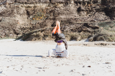 在海滩上做瑜伽的女孩，站在她的头上。