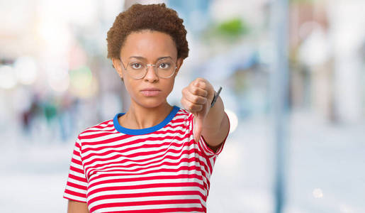 美丽的年轻非洲裔美国妇女戴着眼镜，在孤立的背景上看起来不高兴和愤怒，表现出拒绝和消极的拇指向下的手势。不好的表情。