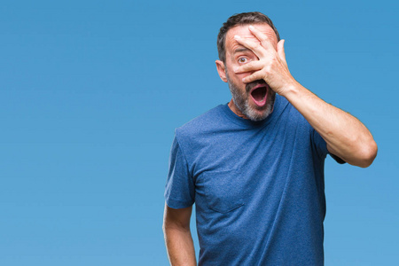 中年老汉在孤立的背景下偷看,震惊地遮住脸和眼睛,用手透过手指看着