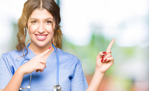 年轻的成年医生女士穿着医疗制服，微笑着看着相机，两只手和手指指向一边。