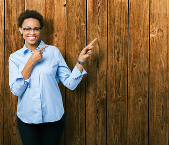 年轻美丽的非裔美国商务妇女在孤立的背景上微笑，看着相机，用两只手和手指指向一边。