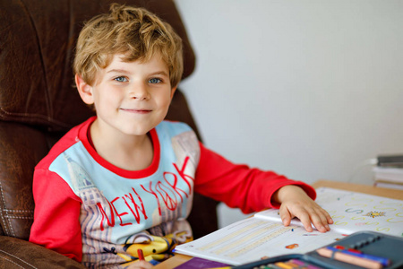 肖像的可爱快乐的学校孩子男孩在家里做家庭作业。用彩色铅笔，在屋里写字的小孩。小学和教育。刚出生的学习写字母和数字