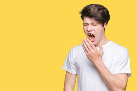 年轻的帅哥穿着休闲的白色t恤,在孤立的背景下无聊地打哈欠,疲惫地用