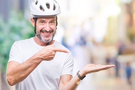中年老人骑自行车的人，穿着自行车安全直升机，孤立的背景，惊讶和微笑的相机，同时呈现手和手指。