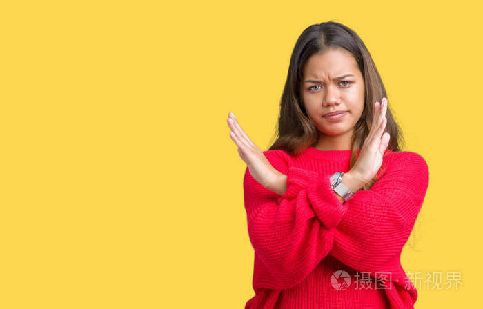 年轻漂亮的黑发女人穿着红色的冬衣在孤立的背景下拒绝表达双臂交叉做
