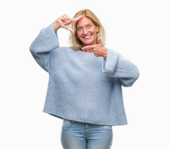 中年金发女人穿着冬天的毛衣，在孤立的背景微笑，用手和手指制作框架，用快乐的脸。 创造力和摄影理念。