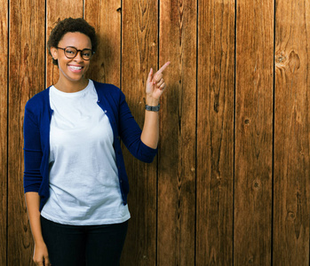 年轻美丽的非裔美国妇女戴着眼镜，在孤立的背景上，脸上挂着一个大大的微笑，用手和手指指向一边，看着相机。