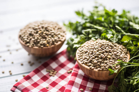未煮熟的扁豆在木制的弓与欧芹草药在厨房的桌子上。