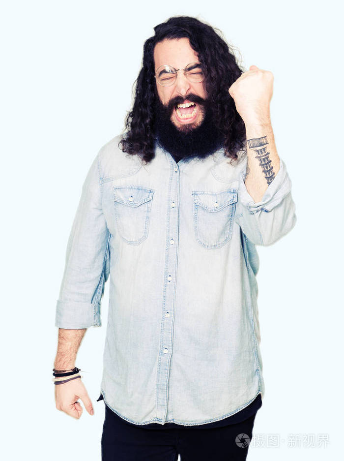 年轻的嬉皮士留着长发和胡须戴着眼镜愤怒而疯狂地举起拳头沮丧而愤怒