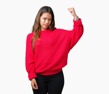 年轻漂亮的深褐色头发的女人穿着红色的冬季毛衣，在孤立的背景下，强壮的人表现出手臂肌肉自信和自豪的力量