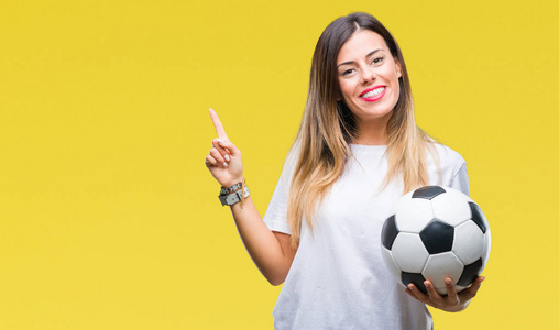 年轻漂亮的女人拿着足球在孤立的背景上，非常高兴地用手和手指指向一边