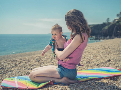 一位年轻的母亲正和她的孩子坐在阳光明媚的夏日海滩上