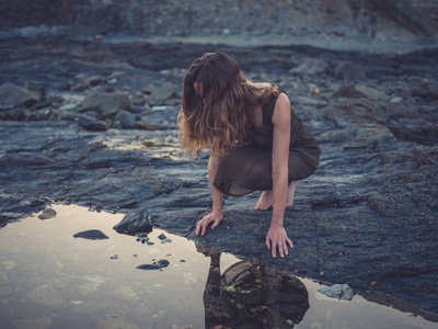 日落时分，一位年轻女子正坐在海岸上的一个岩石池旁