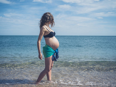 一个穿着纱裙的年轻孕妇站在海滩上